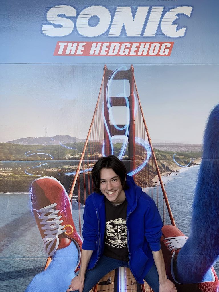 Augie poses in front of the somewhat perverted poster for the Sonic the Hedgehog movie